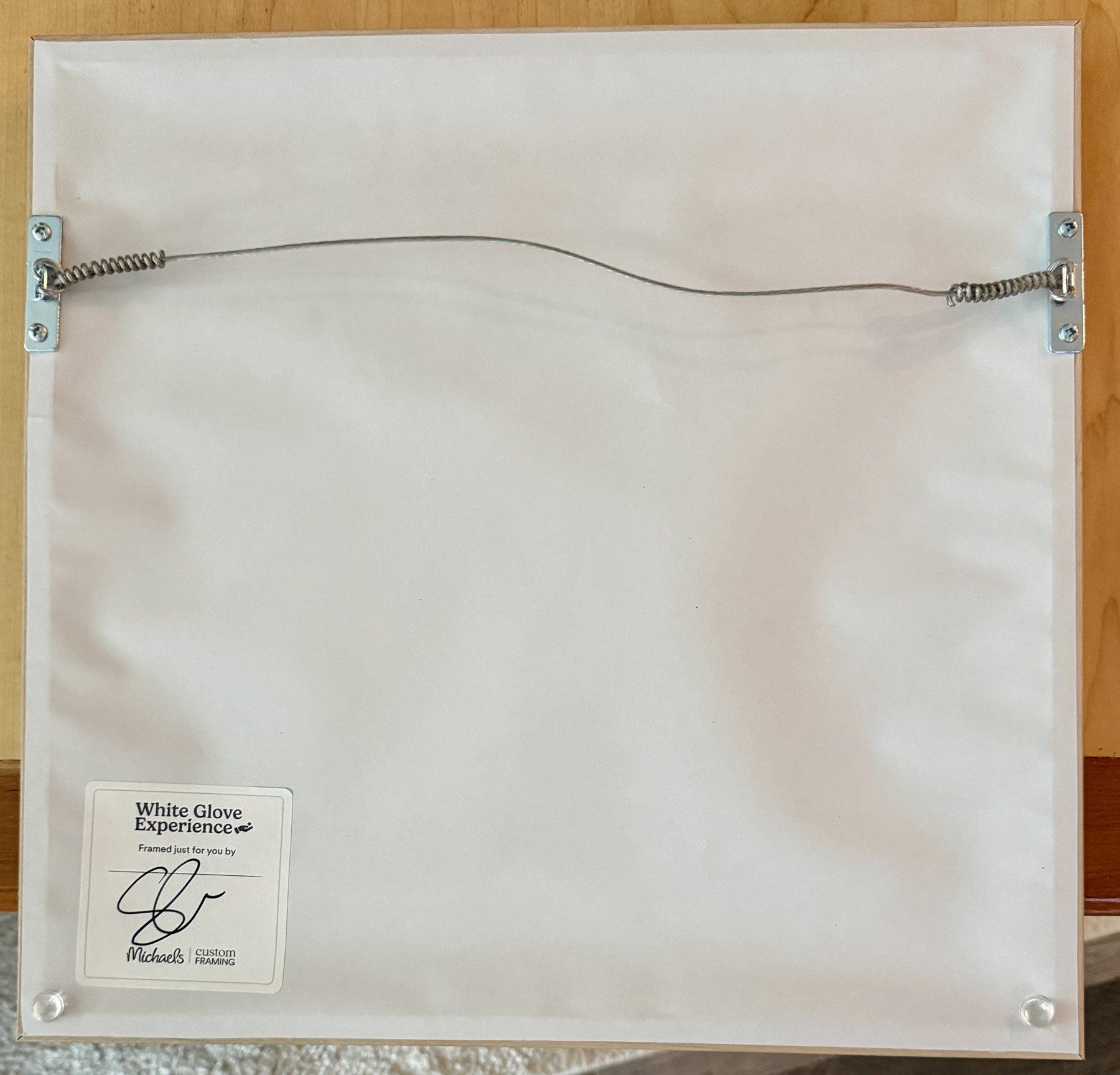 Back of a finished framed artwork showing hanging hardware and finished backing.