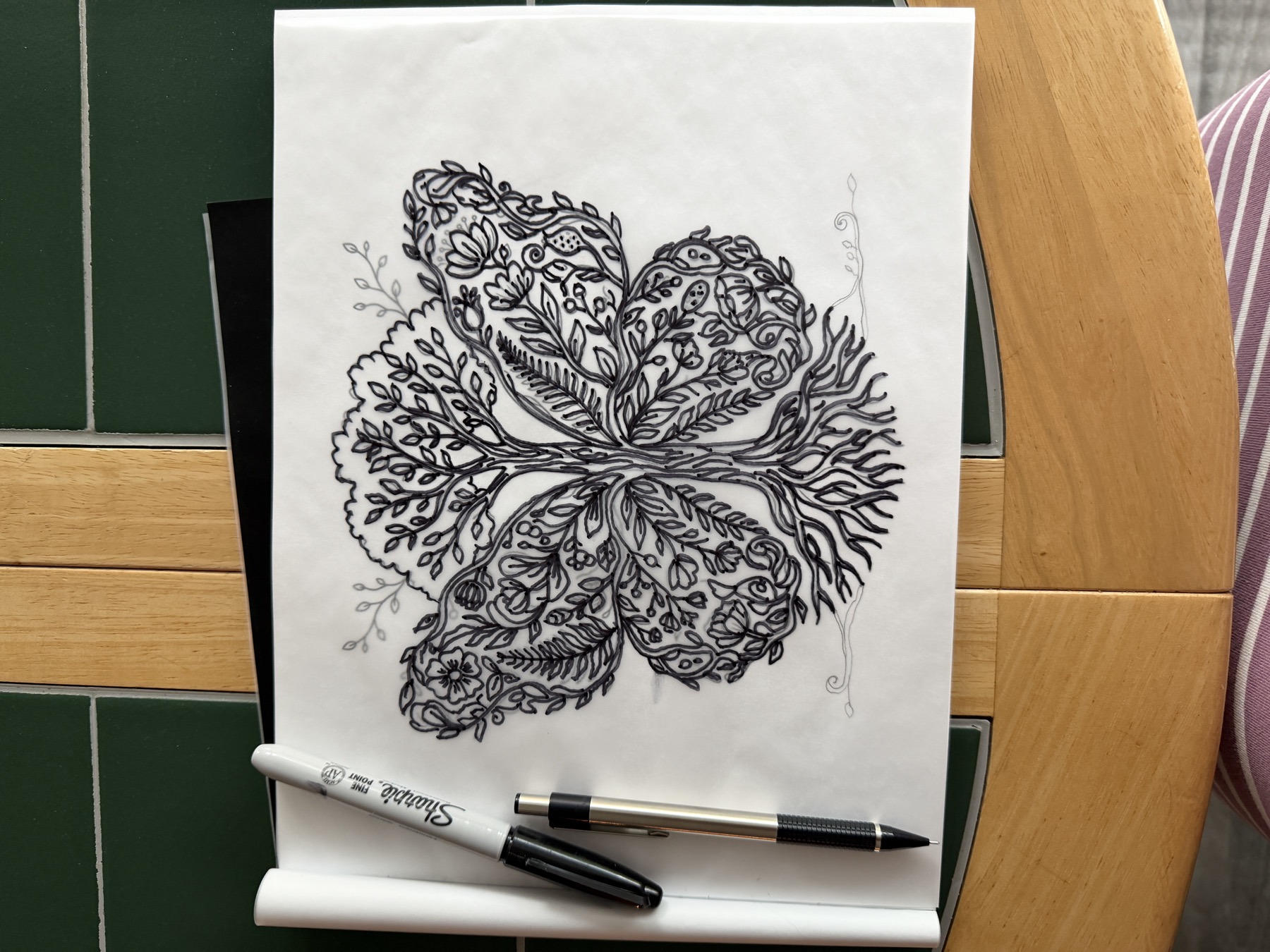 Black ink butterfly tree drawing with a pen and marker beside it.