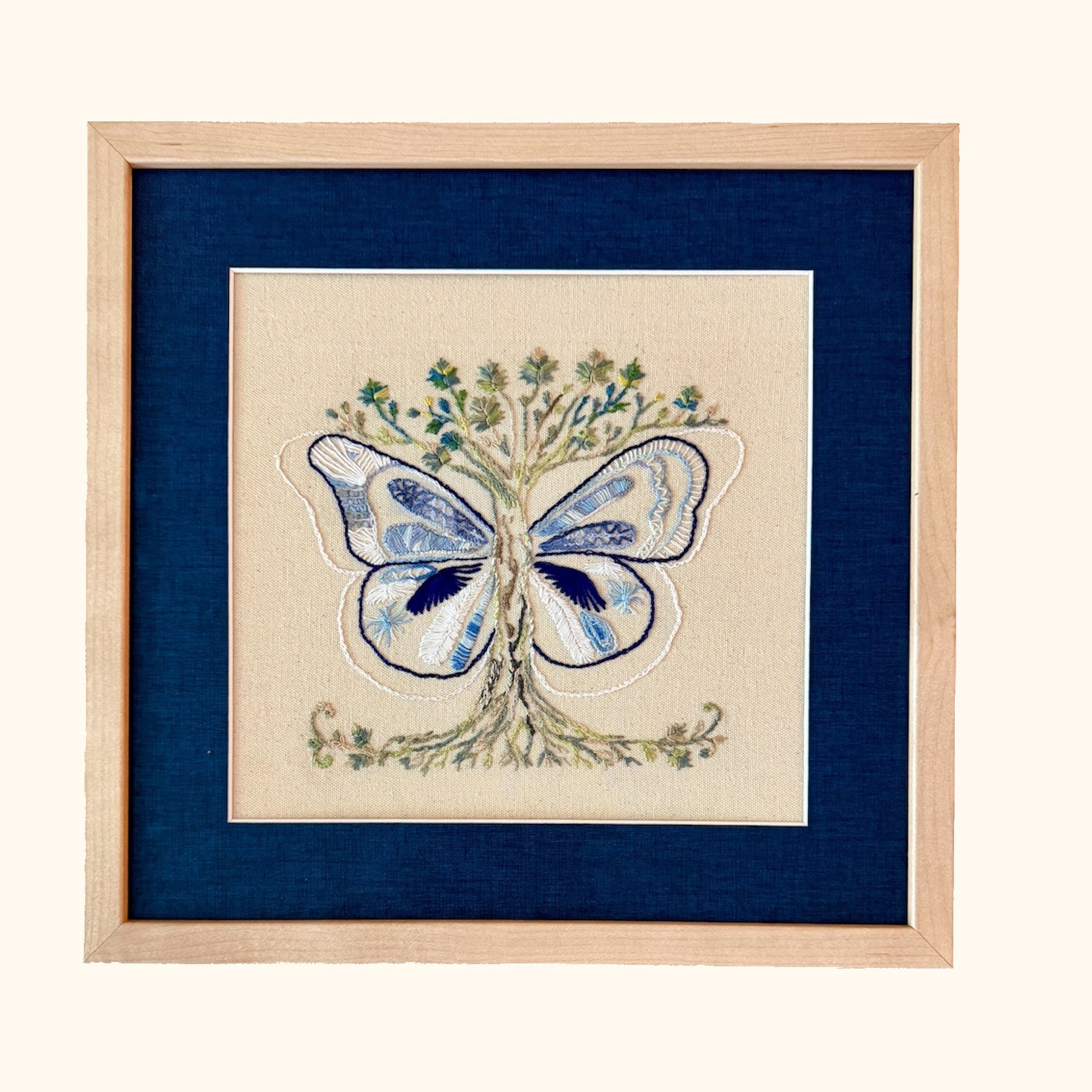 Wild Grace blue butterfly embroidery in a light wood frame with a deep blue mat.